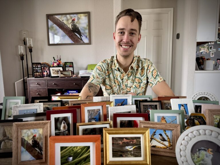 jeff sitting with elbows on the table smiling with assorted mini framed bird photos cover the table